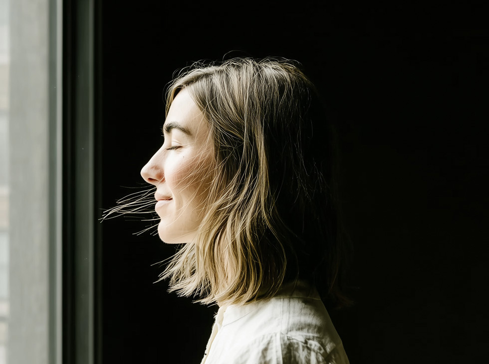 A woman in profile by a window, eyes closed in the light
